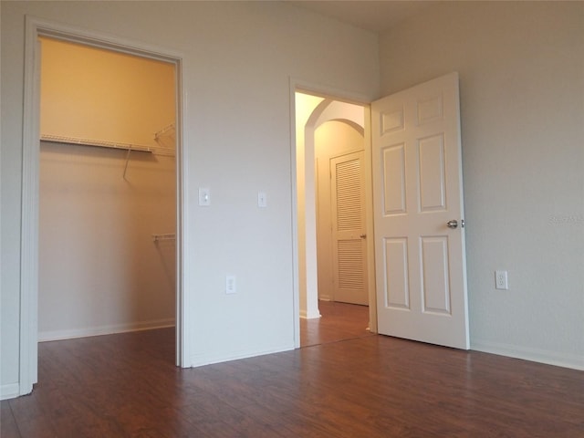 unfurnished bedroom featuring a walk in closet, a closet, and dark wood-type flooring