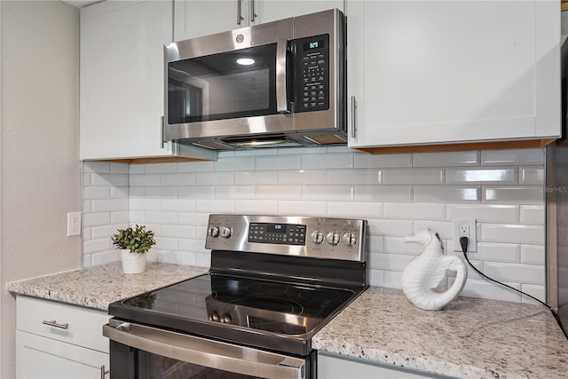 kitchen featuring white cabinets, backsplash, stainless steel appliances, and light stone countertops