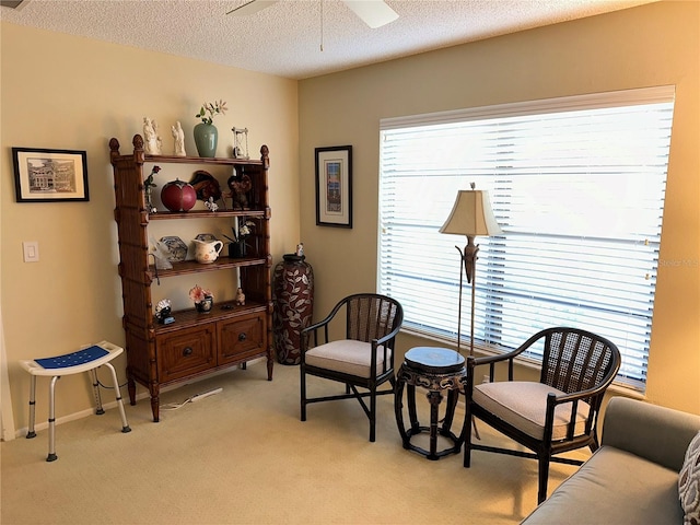 living area with light carpet, ceiling fan, and a textured ceiling