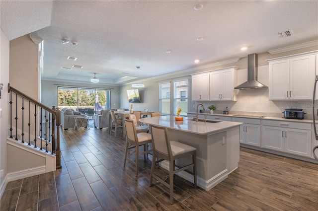 kitchen with white cabinetry, sink, wall chimney exhaust hood, dark hardwood / wood-style flooring, and an island with sink