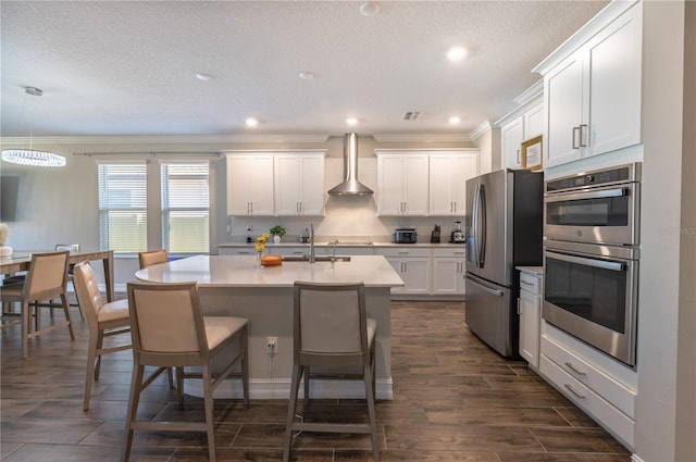 kitchen featuring wall chimney exhaust hood, white cabinetry, stainless steel appliances, and hanging light fixtures