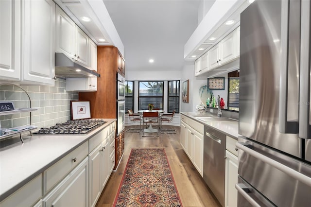 kitchen with white cabinets, backsplash, light hardwood / wood-style floors, and stainless steel appliances