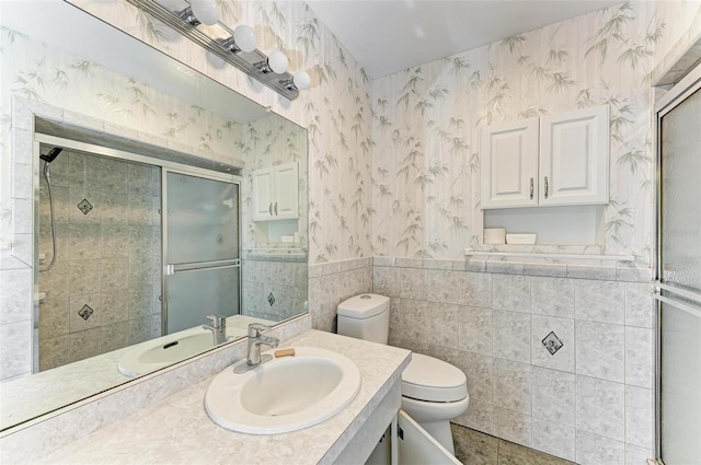 bathroom featuring a shower with door, vanity, tile walls, and toilet