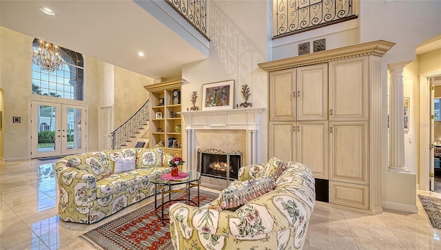 living room with french doors, ornate columns, an inviting chandelier, a premium fireplace, and a high ceiling