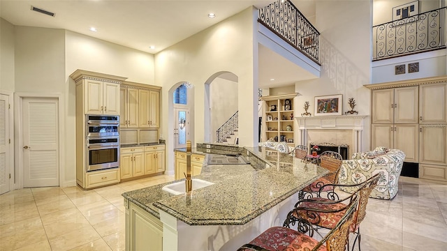 kitchen featuring a high ceiling, double oven, a breakfast bar area, and dark stone countertops