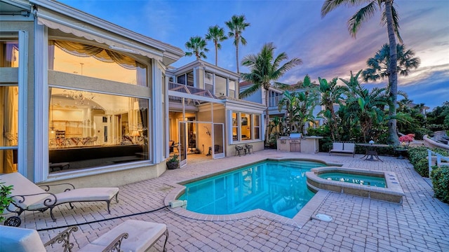 pool at dusk featuring an in ground hot tub and a patio