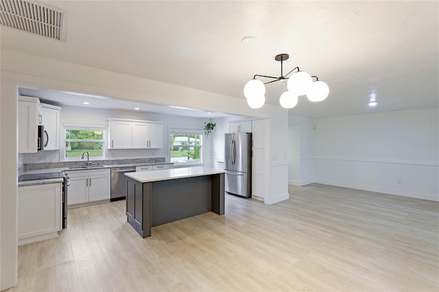 kitchen with light wood-type flooring, stainless steel appliances, pendant lighting, a center island, and white cabinetry