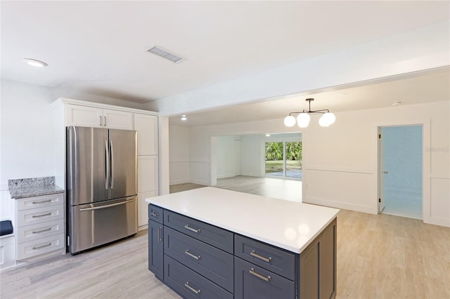 kitchen with decorative light fixtures, light wood-type flooring, white cabinetry, and stainless steel refrigerator