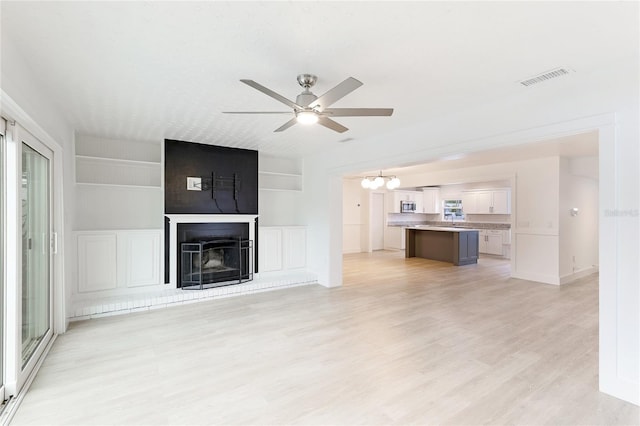 unfurnished living room featuring ceiling fan with notable chandelier, built in features, light wood-type flooring, and a fireplace