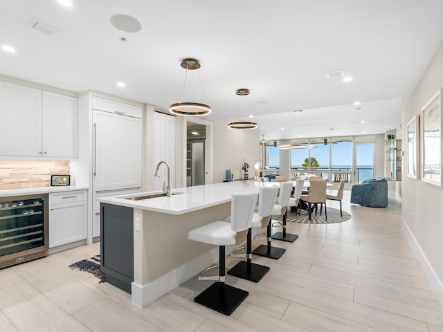 kitchen with decorative light fixtures, white cabinetry, sink, beverage cooler, and a water view