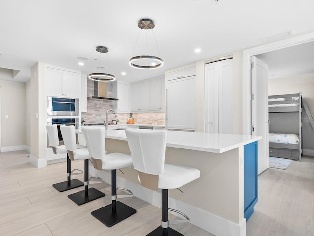 kitchen featuring a kitchen bar, white cabinetry, tasteful backsplash, an island with sink, and pendant lighting