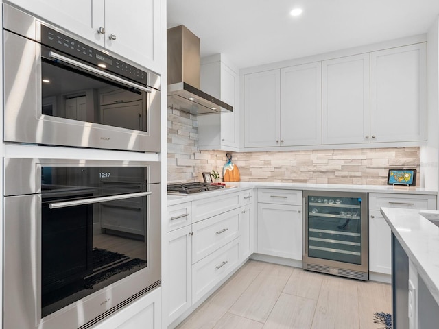 kitchen with wine cooler, wall chimney range hood, and white cabinetry