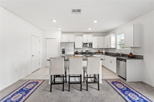 kitchen with a kitchen bar, appliances with stainless steel finishes, light tile patterned floors, white cabinets, and a kitchen island