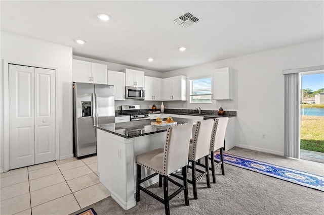 kitchen with stainless steel appliances, light tile patterned floors, a kitchen island, a kitchen breakfast bar, and white cabinets