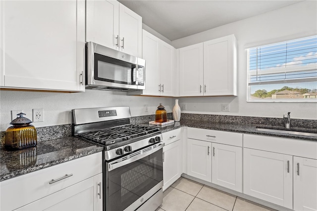 kitchen featuring dark stone counters, stainless steel appliances, sink, light tile patterned floors, and white cabinets