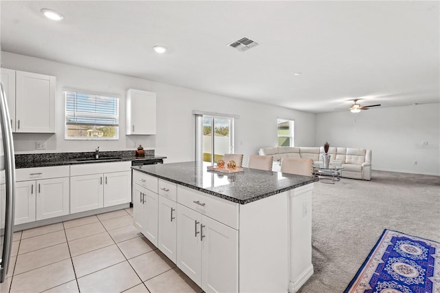 kitchen with white cabinets, a kitchen island, sink, and light carpet