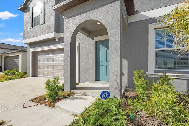 doorway to property with driveway, an attached garage, and stucco siding