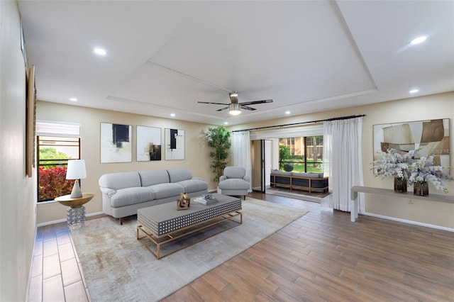 living room featuring wood-type flooring, a tray ceiling, and ceiling fan