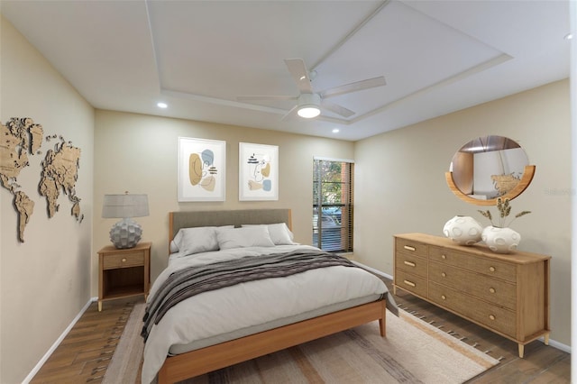 bedroom with ceiling fan, dark hardwood / wood-style flooring, and a tray ceiling