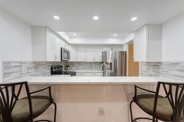 kitchen with kitchen peninsula, a breakfast bar, white cabinets, and appliances with stainless steel finishes