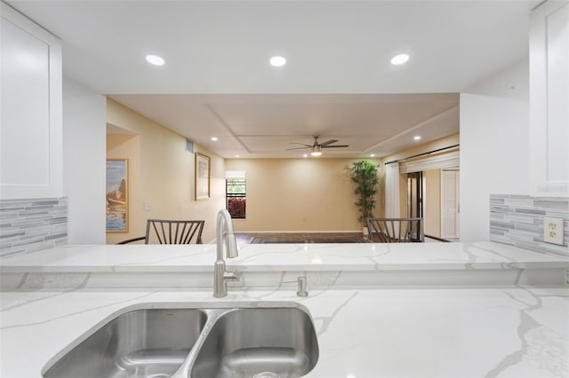 kitchen with white cabinets, backsplash, light stone counters, and sink