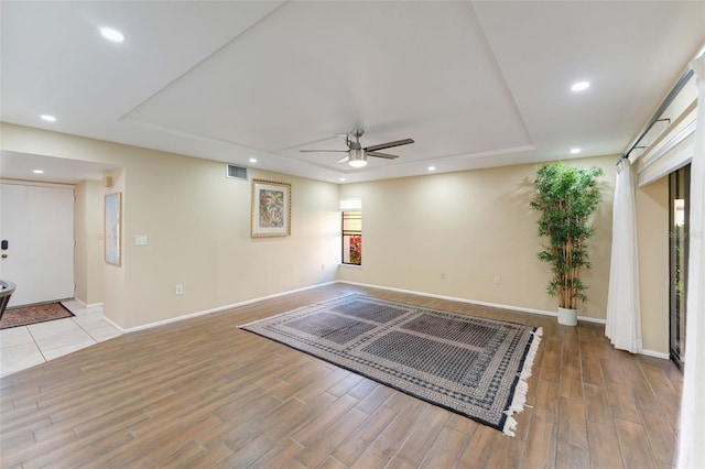 interior space with a raised ceiling, ceiling fan, and light wood-type flooring