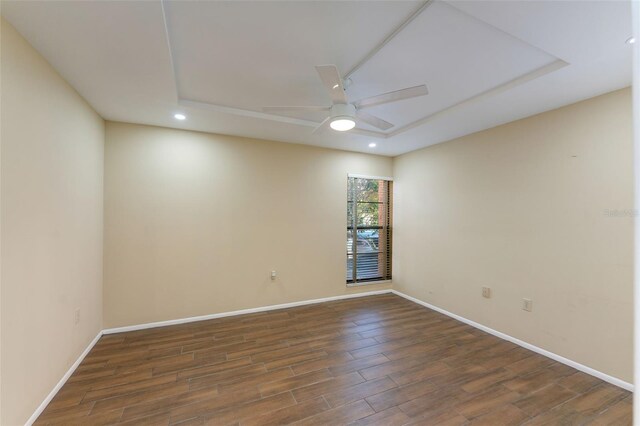 empty room with a raised ceiling, ceiling fan, and dark wood-type flooring