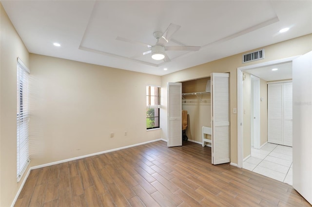 unfurnished bedroom with ceiling fan, light hardwood / wood-style floors, a raised ceiling, and a closet