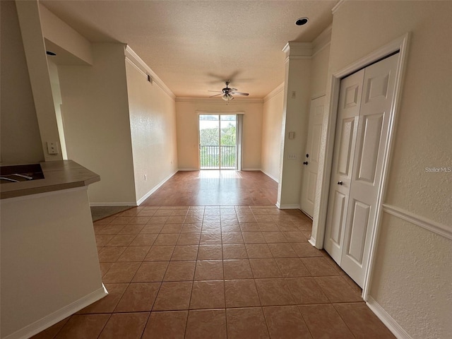 tiled empty room featuring a textured ceiling, ceiling fan, and crown molding