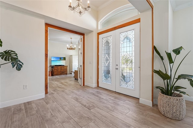 entrance foyer featuring an inviting chandelier, light wood-type flooring, ornamental molding, and french doors