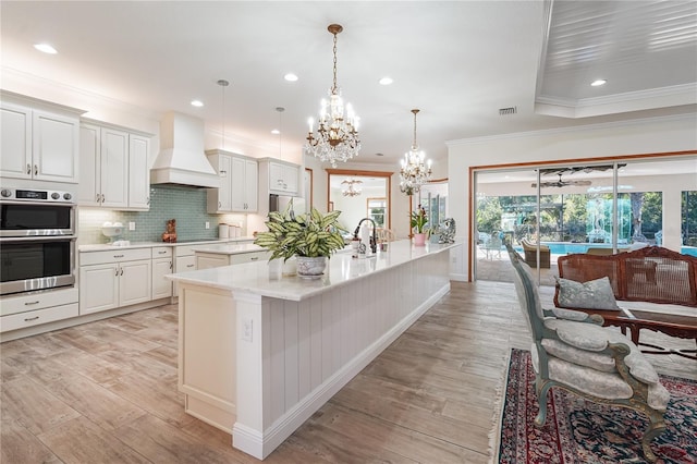 kitchen featuring white cabinets, decorative backsplash, premium range hood, and double oven