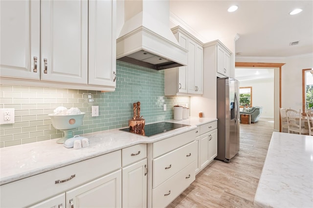 kitchen with stainless steel fridge, black electric stovetop, premium range hood, and white cabinetry