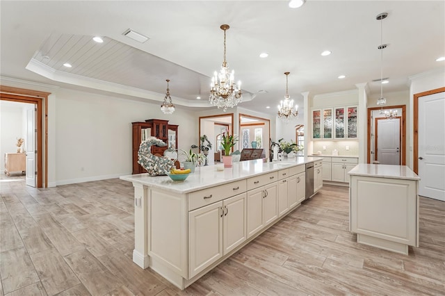 kitchen featuring dishwasher, hanging light fixtures, an island with sink, a tray ceiling, and ornamental molding