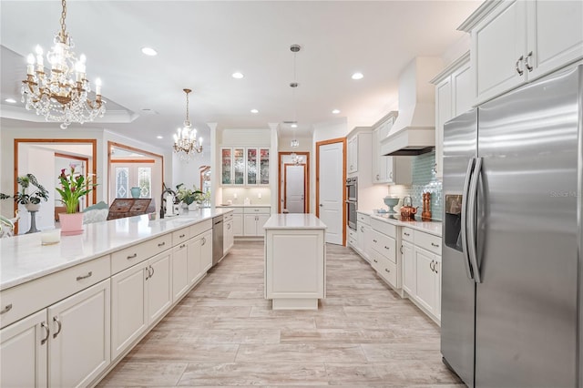 kitchen with appliances with stainless steel finishes, tasteful backsplash, custom range hood, decorative light fixtures, and a kitchen island