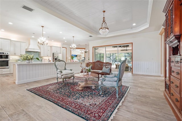 living room with a tray ceiling, an inviting chandelier, and crown molding