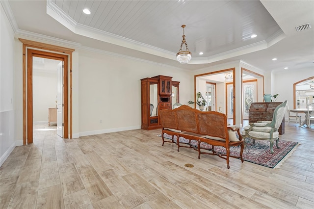 living area featuring a raised ceiling, an inviting chandelier, ornamental molding, and light wood-type flooring