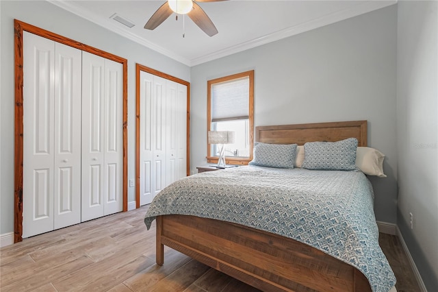 bedroom featuring ceiling fan, light hardwood / wood-style floors, two closets, and ornamental molding