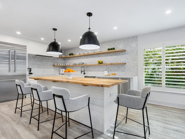 kitchen featuring butcher block countertops, a breakfast bar, light wood-type flooring, and tasteful backsplash