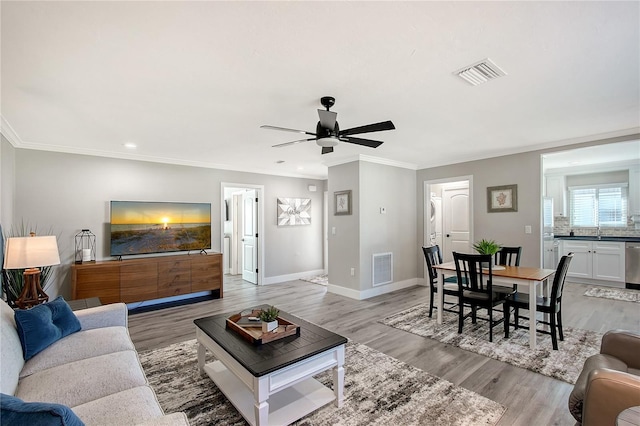 living room featuring ceiling fan, sink, crown molding, and light hardwood / wood-style flooring