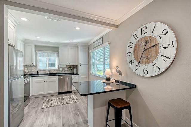 kitchen with decorative backsplash, appliances with stainless steel finishes, crown molding, light hardwood / wood-style floors, and white cabinetry