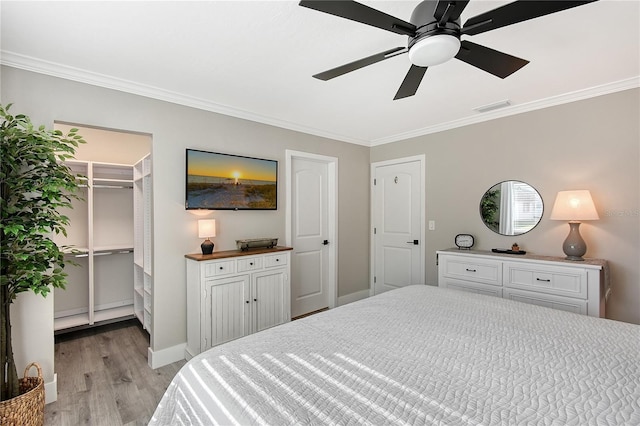 bedroom featuring ceiling fan, a walk in closet, ornamental molding, and light hardwood / wood-style flooring