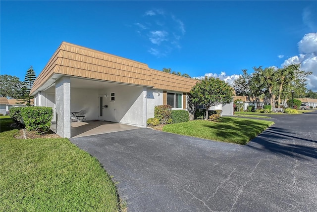 view of front of home featuring a front lawn, aphalt driveway, stucco siding, mansard roof, and a carport