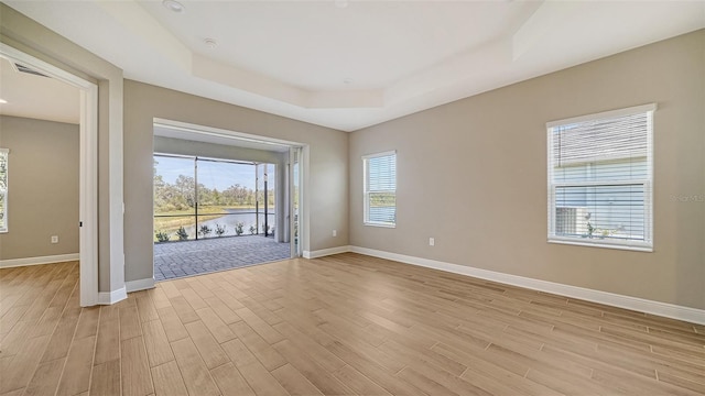 unfurnished room with a healthy amount of sunlight, a raised ceiling, and light hardwood / wood-style floors