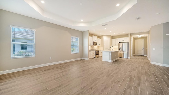 unfurnished living room featuring light wood-type flooring, a raised ceiling, a wealth of natural light, and sink