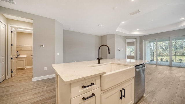 kitchen with sink, light stone counters, light wood-type flooring, and a kitchen island with sink