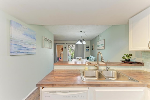 kitchen featuring white dishwasher, sink, hanging light fixtures, a notable chandelier, and white cabinetry