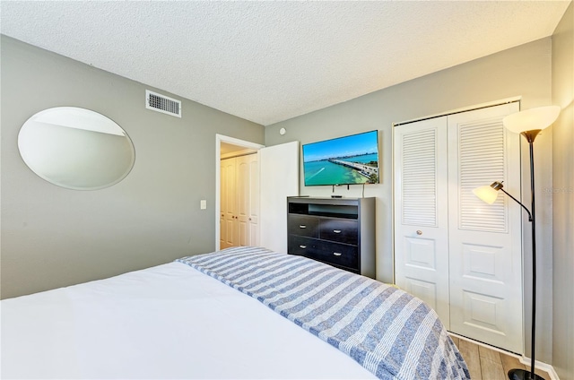 bedroom with light wood-type flooring, a textured ceiling, and a closet