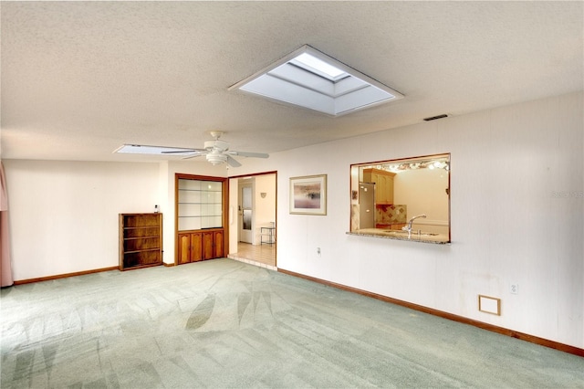 spare room with a skylight, ceiling fan, light colored carpet, and a textured ceiling