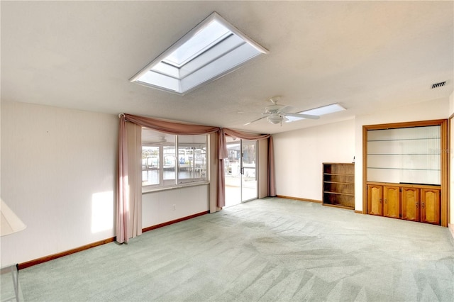 unfurnished living room featuring a skylight, ceiling fan, and light colored carpet