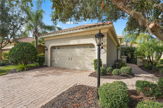 exterior space featuring decorative driveway, a tiled roof, an attached garage, and stucco siding